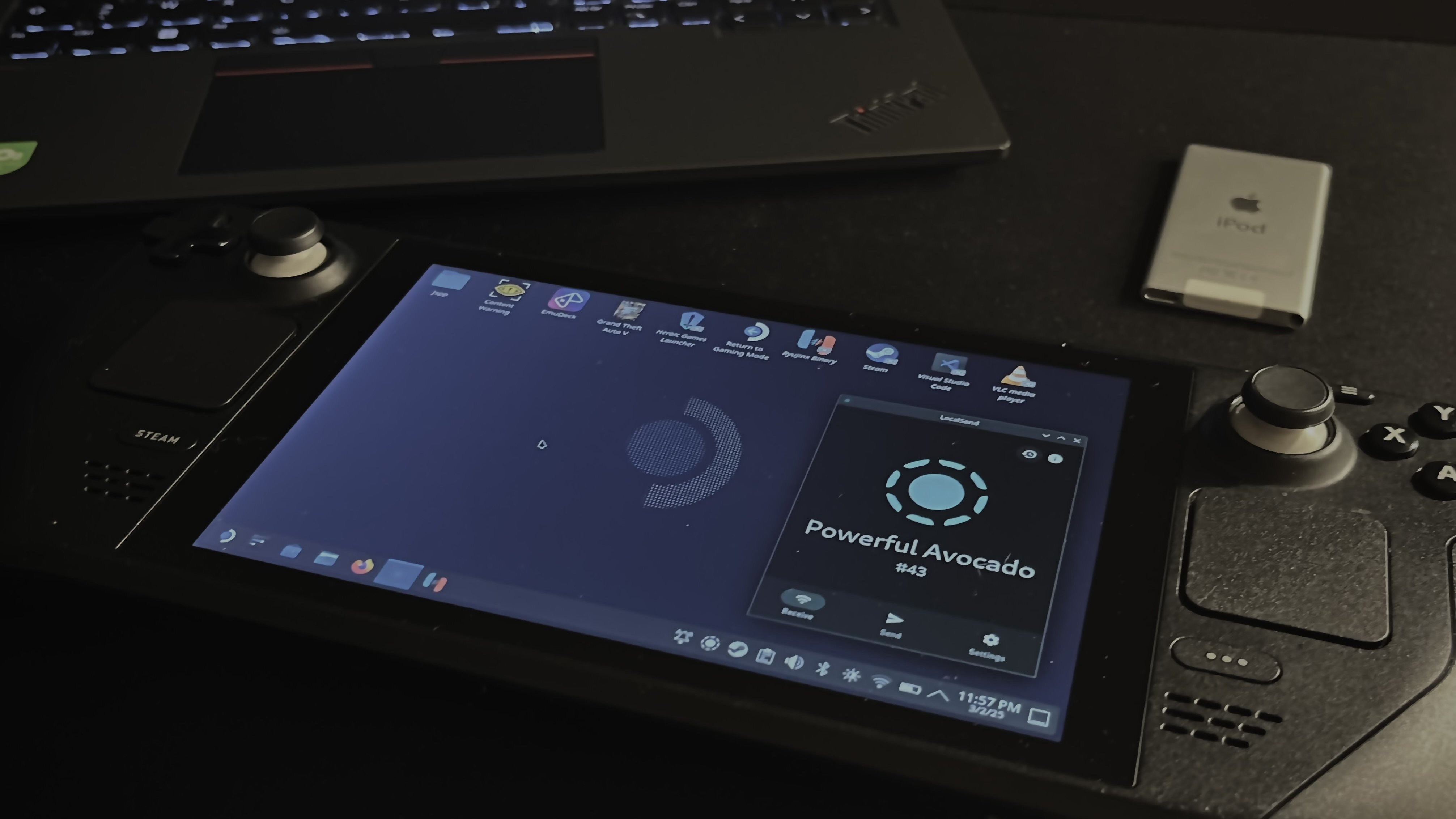 Steam Deck running a Linux desktop interface with a laptop and iPod nearby