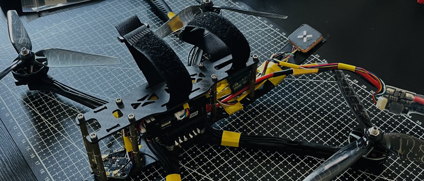 The real MaxFly V0 drone mid-build on a cutting mat — an open-prop frame with a flight controller, GPS module and long-range radio wired up on the bench